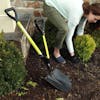 Sun Joe 9-inch Green Shovelution Strain-Reducing Utility Round-Point Digging Garden Shovel in a garden while a woman plants a small bush.