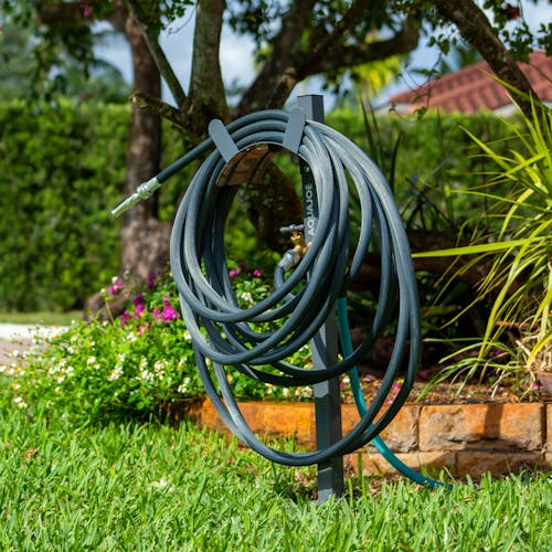 Aqua Joe Gray Garden Hose Stand with Brass Faucet placed in a lawn holding a garden hose.