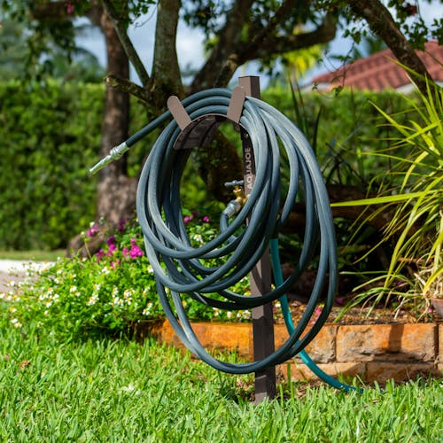 Aqua Joe Tan Garden Hose Stand with Brass Faucet placed in a lawn holding a hose.