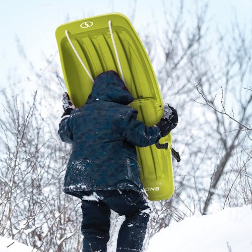 Kid carrying the Snow Joe 34-inch green-colored kids snow sled up a hill.