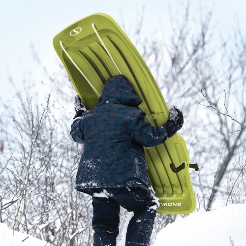 Kid carrying the Snow Joe 48-inch green-colored kids snow sled up a hill.