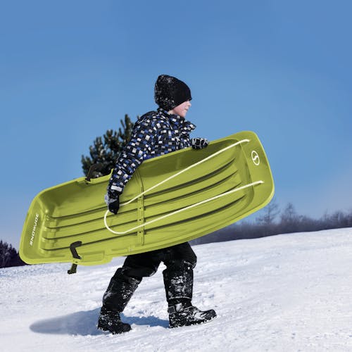 Kid carrying the Snow Joe 48-inch green-colored kids snow sled.