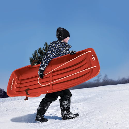Kid carrying the Snow Joe 48-inch red-colored kids snow sled.