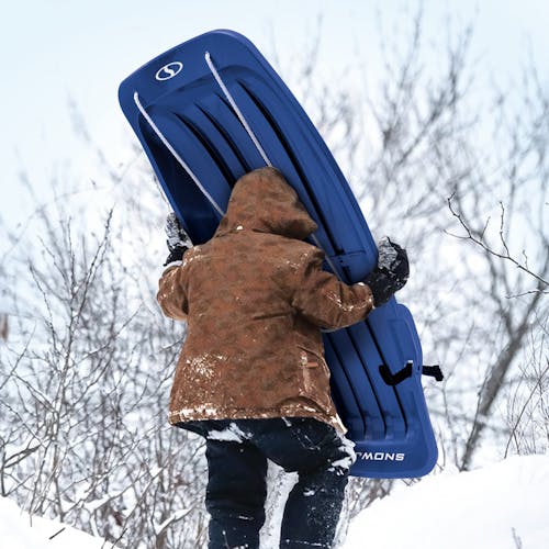 Kid carrying the Snow Joe 48-inch blue-colored kids snow sled up a hill.