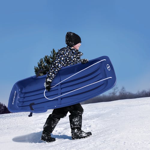 Kid carrying the Snow Joe 48-inch blue-colored kids snow sled.