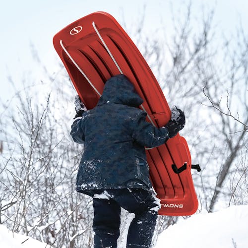 Kid carrying the Snow Joe 48-inch red-colored kids snow sled up a hill.