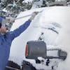Snow Joe 2-pack of 4-in-1 telescoping gray-colored snow broom and ice scraper with LED light being used to push snow off the top of a car.