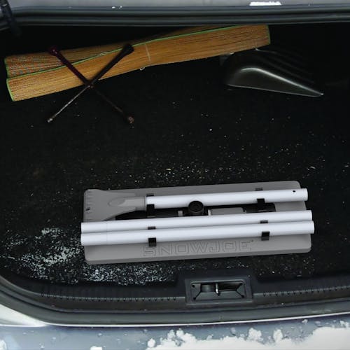 Snow Joe 18-inch 3-in-1 gray-colored telescoping snow broom and ice scraper with an LED light collapsed in the trunk of a car.