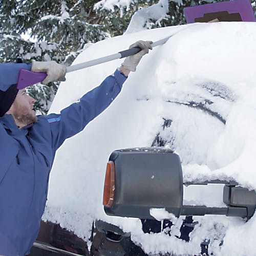 Snow Joe 18-inch 3-in-1 purple-colored telescoping snow broom and ice scraper with an LED light pushing snow off the top of a car.