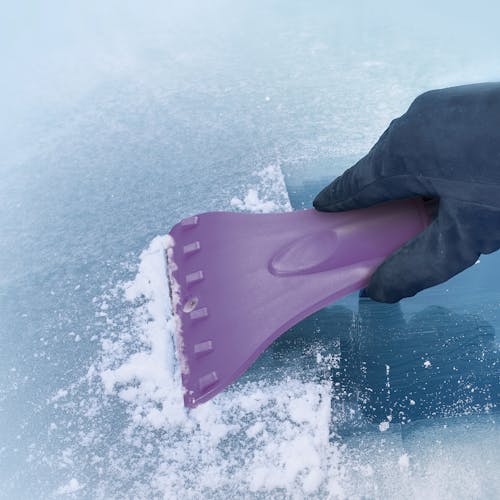Snow Joe 18-inch 3-in-1 purple-colored telescoping snow broom and ice scraper with an LED light scraping ice off a window.