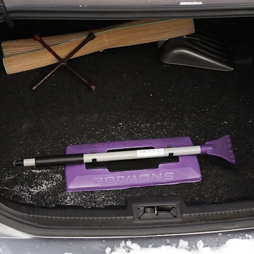 Snow Joe 19-inch 2-In-1 Telescoping purple Snow Broom and Ice Scraper compacted and stored in the trunk of a car.