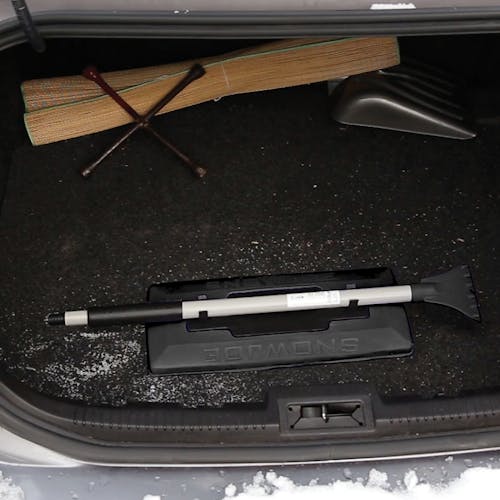 Snow Joe 19-inch 2-In-1 Telescoping black Snow Broom and Ice Scraper compacted and stored in a car trunk.