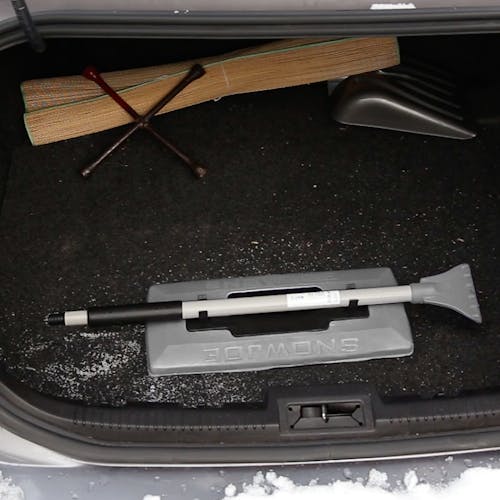 Snow Joe 19-inch 2-In-1 Telescoping gray Snow Broom and Ice Scraper compacted and stored in a car trunk.