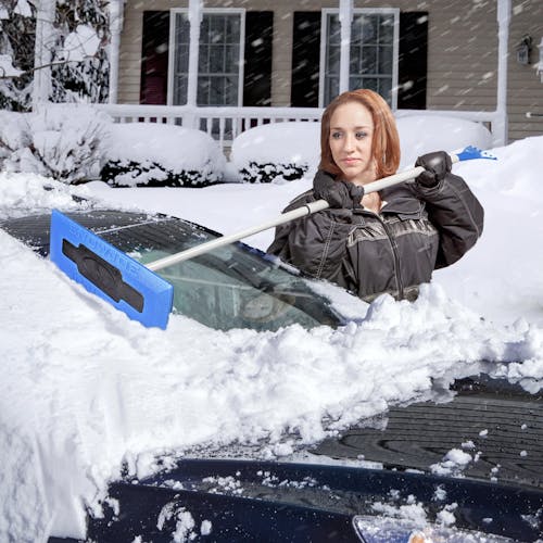 Woman clearing the windshield of a car with the snow broom.