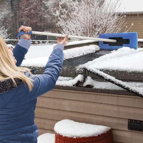 Woman using the snow broom to clear off the top of a shed.