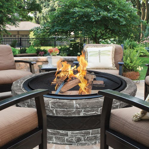 Sun Joe 28-Inch Charcoal Gray Cast Stone Base, Wood Burning 24-Inch Fire Pit with a fire going and patio furniture around it.