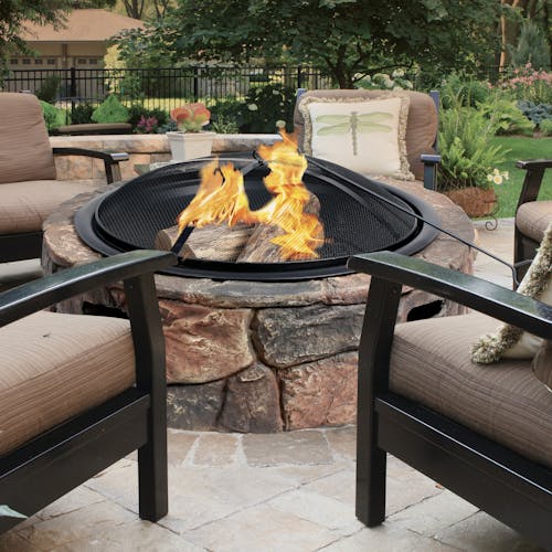 Fire going in the Sun Joe 35-inch Large Cast Stone Base, Wood Burning Fire Pit with patio chairs around it.