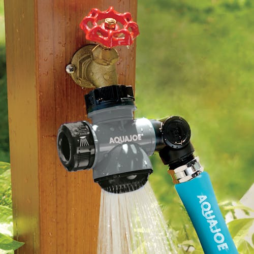 Aqua Joe Multi-Function gray-colored Outdoor Faucet and Garden Hose Tap Connector spraying water with a garden hose attached.