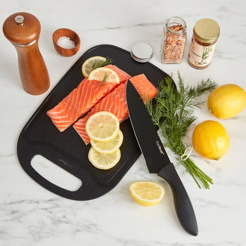 Fish and lemons on the cutting board with a chefs knife on the kitchen counter.