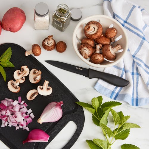Onions and mushrooms on the cutting board with a utility knife on a kitchen counter.