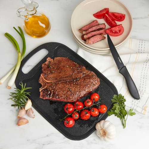 Steak and tomatoes on the cutting board with the steak knife on the kitchen counter.