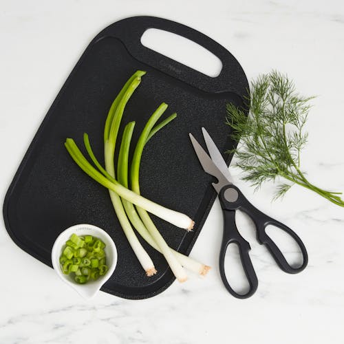Kitchen scissors being used to cut celery on the cutting board.