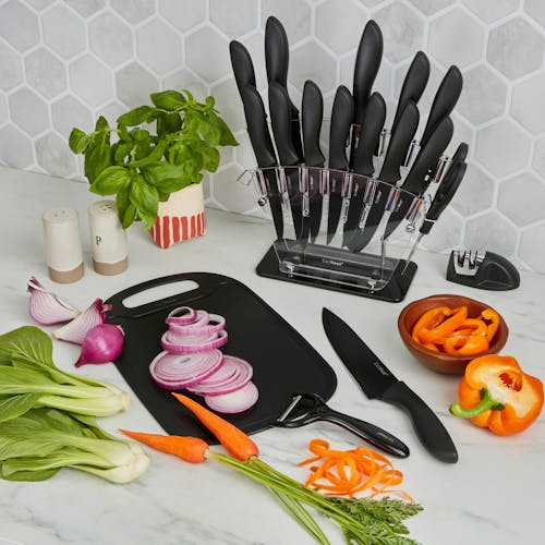 Vegetables on the cutting board with a chefs knife and peeler beside it, and the knife holder behind it.