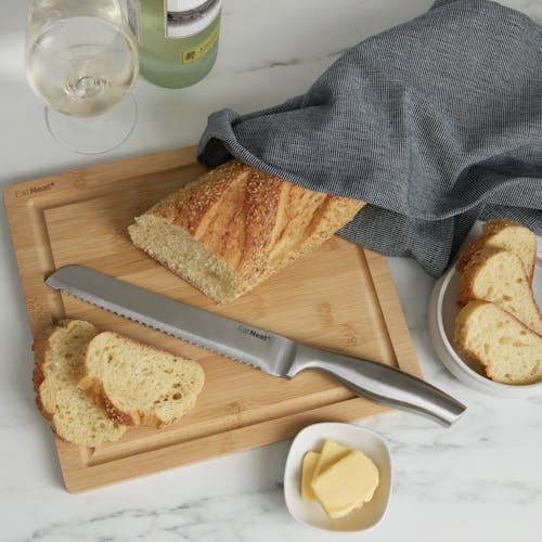 Cutting board for the EatNeat 8-piece knife set with a knife and loaf of bread on it with butter and wine next to it on the kitchen counter.