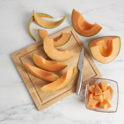 Cutting board for the EatNeat 8-piece knife set with a knife and cantaloupe on it.