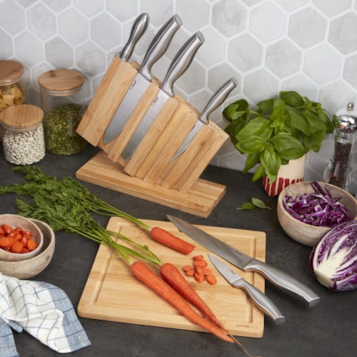 Cutting board for the EatNeat 8-piece knife set with a knife and carrots on it. The knife block is behind it holding 3 knives.