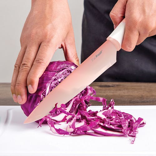 Pale pink chef's knife being used to cut an onion.