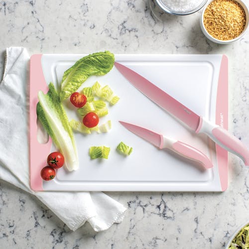 2 pale pink knives on the cutting board along with lettuce and tomatoes.