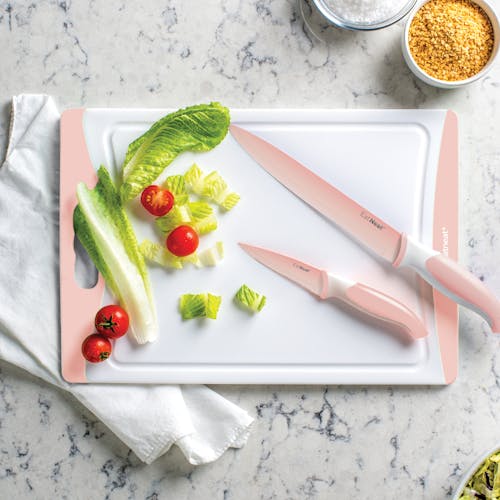 2 pale pink knives on the cutting board along with lettuce and tomatoes.