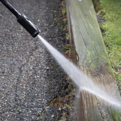 Spray wand being used to clean a wooden curb on the side of a driveway.