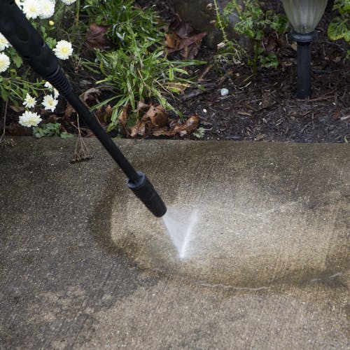 Spray wand being used to clean dirt off of cement.