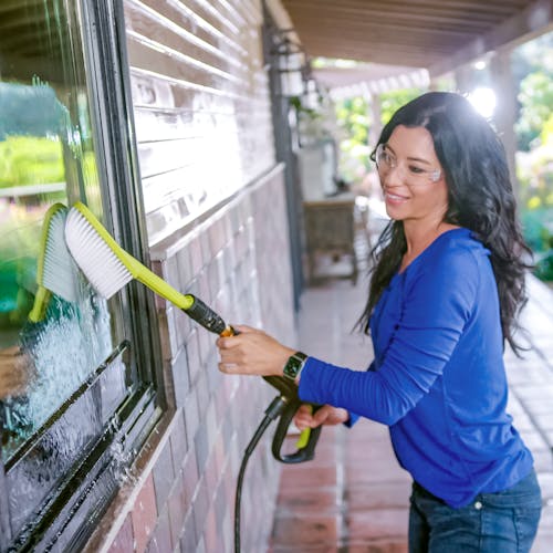Woman using the utility brush for SPX series pressure washers to clean the windows of a house.