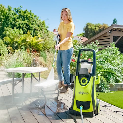Sun Joe 13-amp 2200 PSI Extreme Clean Electric Pressure Washer being used to clean a small table on a deck.