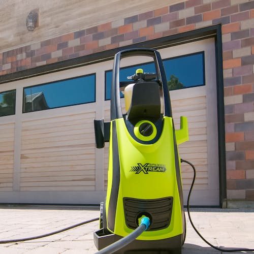 Sun Joe 13-amp 2200 PSI Extreme Clean Electric Pressure Washer in a driveway in fton of the garage.