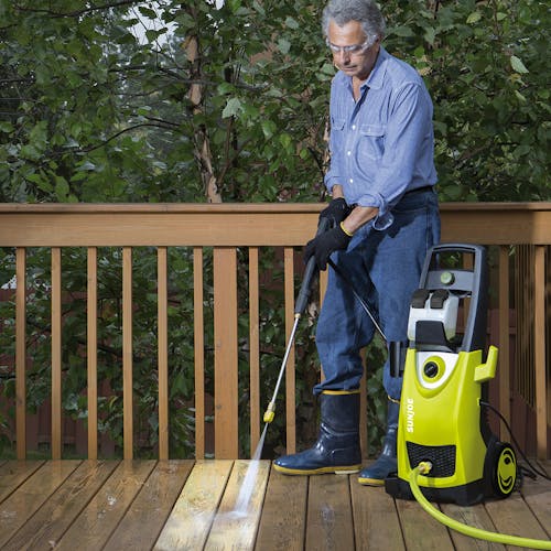 Man using the Sun Joe 14.5-amp 2030 PSI Electric Pressure Washer to clean a wooden deck.