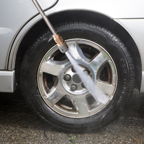Spray wand being used to clean the rims of a tire on a car.