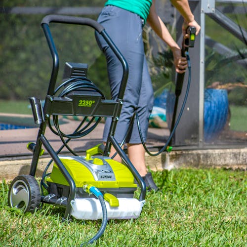 Sun Joe 14.5-amp 2250 PSI Electric Pressure Washer. being used to wash a curb in a backyard.