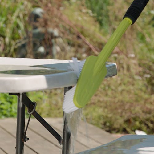 Sun Joe Feather Bristle Utility Brush for SPX Series Pressure Washers being used to clean a patio table.