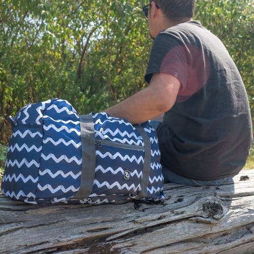 TrailGear 20-liter sky blue transparent dry bag next to a man on a log.