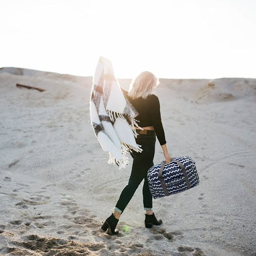 Girl carrying the TrailGear 20-liter sky blue transparent dry bag on a beach.