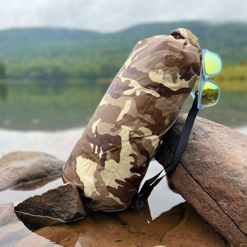 TrailGear 10-liter brown camo dry bag leaning against a log in shallow water.
