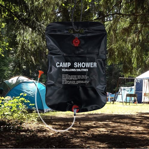 TrailGear 20-liter solar shower bag hanging from a tree with a camp in the background.