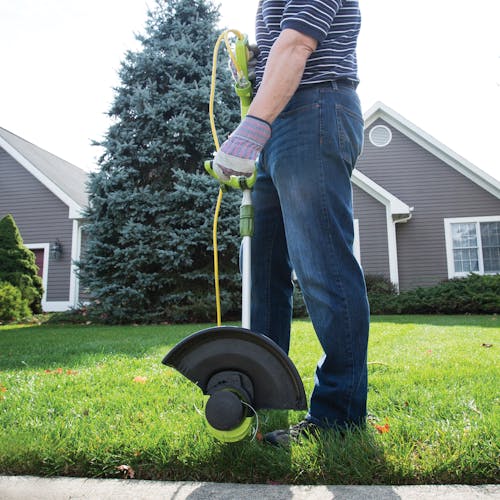 Person using the Sun Joe 4-amp 13-inch Electric String Grass Trimmer to trim the edges of a lawn.
