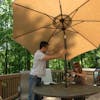 Man tilting the top of the 9-foot tan patio umbrella on a back deck.