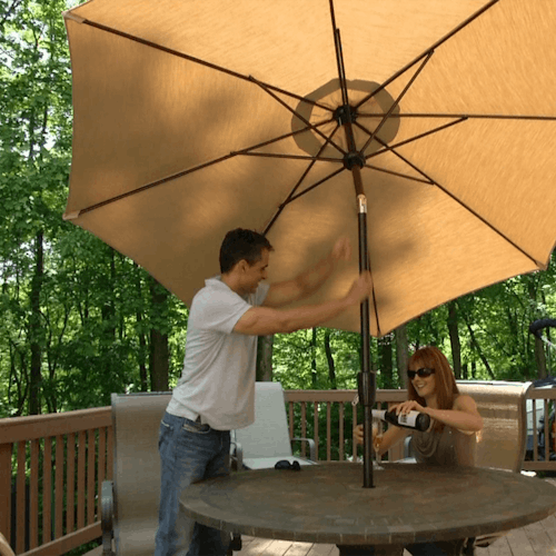 Man tilting the top of the 9-foot tan patio umbrella on a back deck.