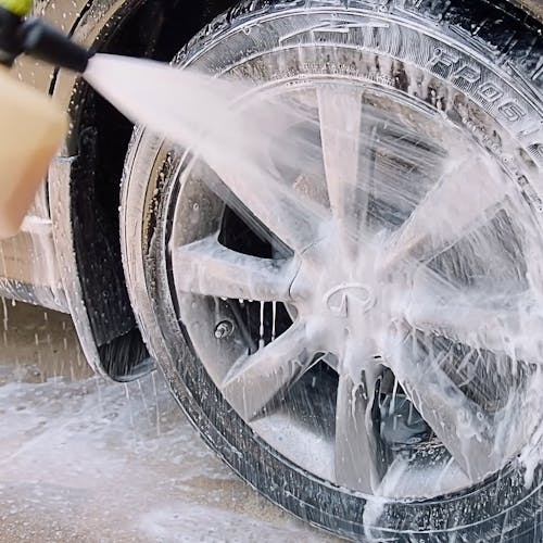 Sun Joe pressure washer detergent being used to wash the wheels of a car.